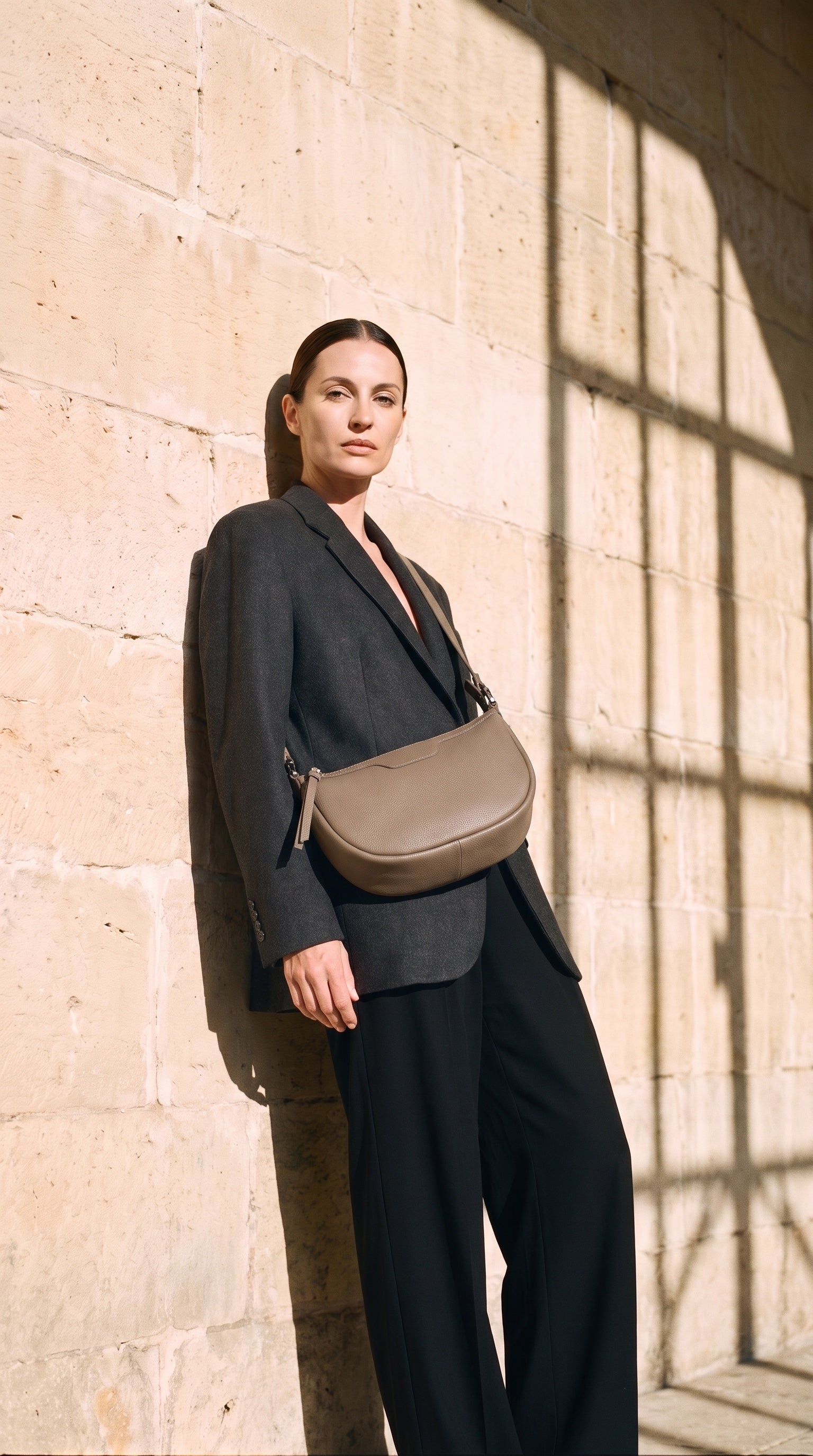 Sac HALFMOON porté par le mannequin devant un mur de pierre