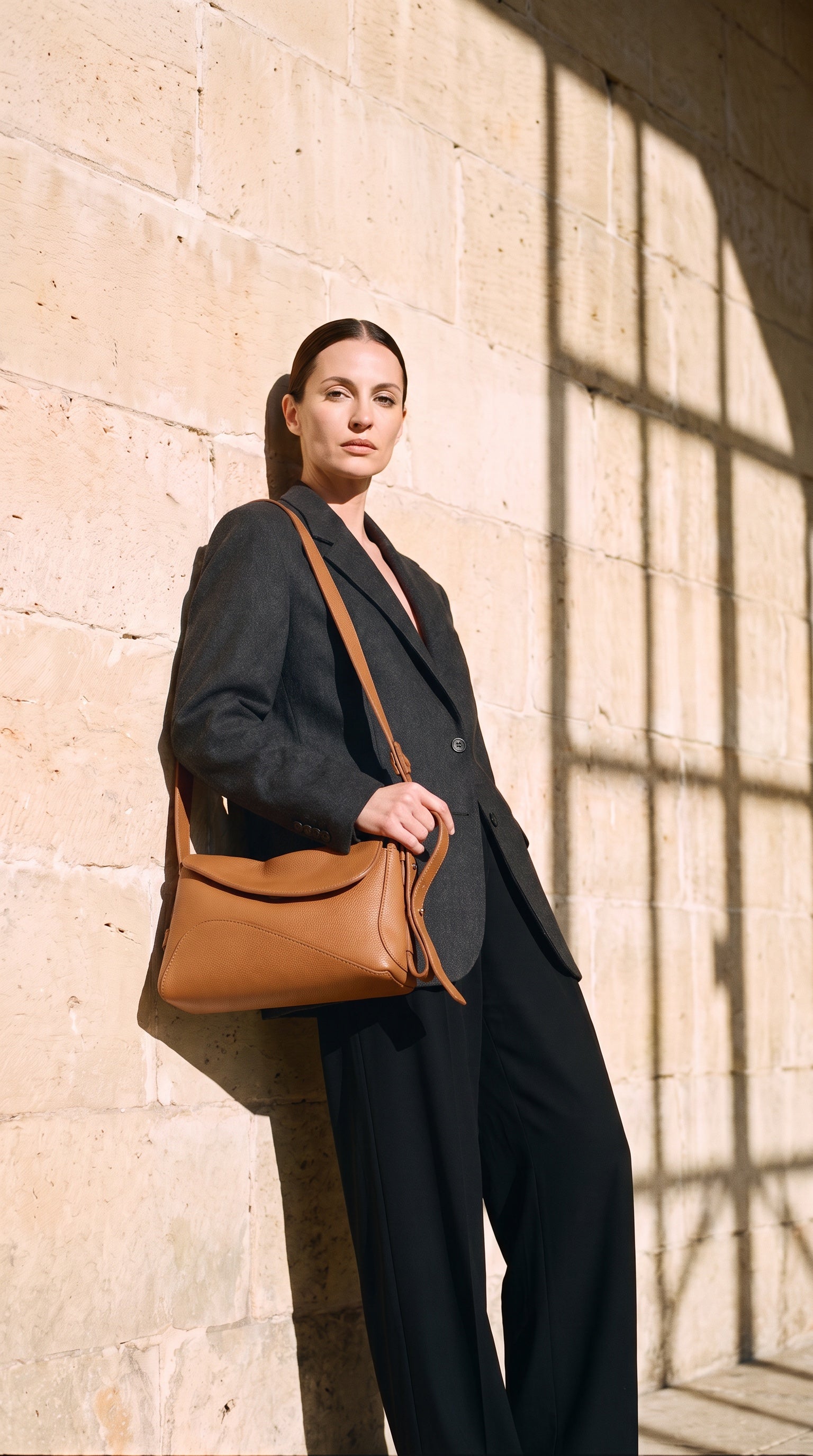Sac NINA porté par le mannequin devant un mur de pierre